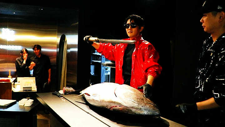 The host raises the long tuna knife over a whole bluefin tuna