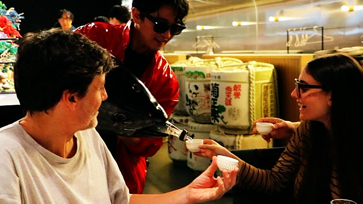 マグロの頭から注がれる日本酒を受けるゲスト